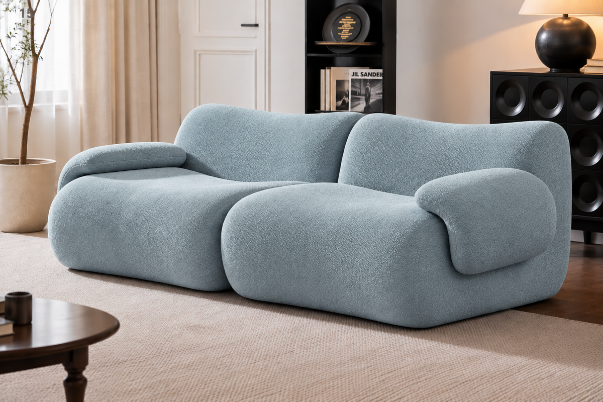 A modern light blue boucle sofa with rounded, organic shapes, styled in a contemporary living room setting with a beige rug, wooden coffee table, and shelving in the background.