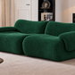 A modern, low-profile sofa upholstered in a textured dark green boucle fabric, styled in a contemporary living room setting with a beige rug, wooden coffee table, and shelving.