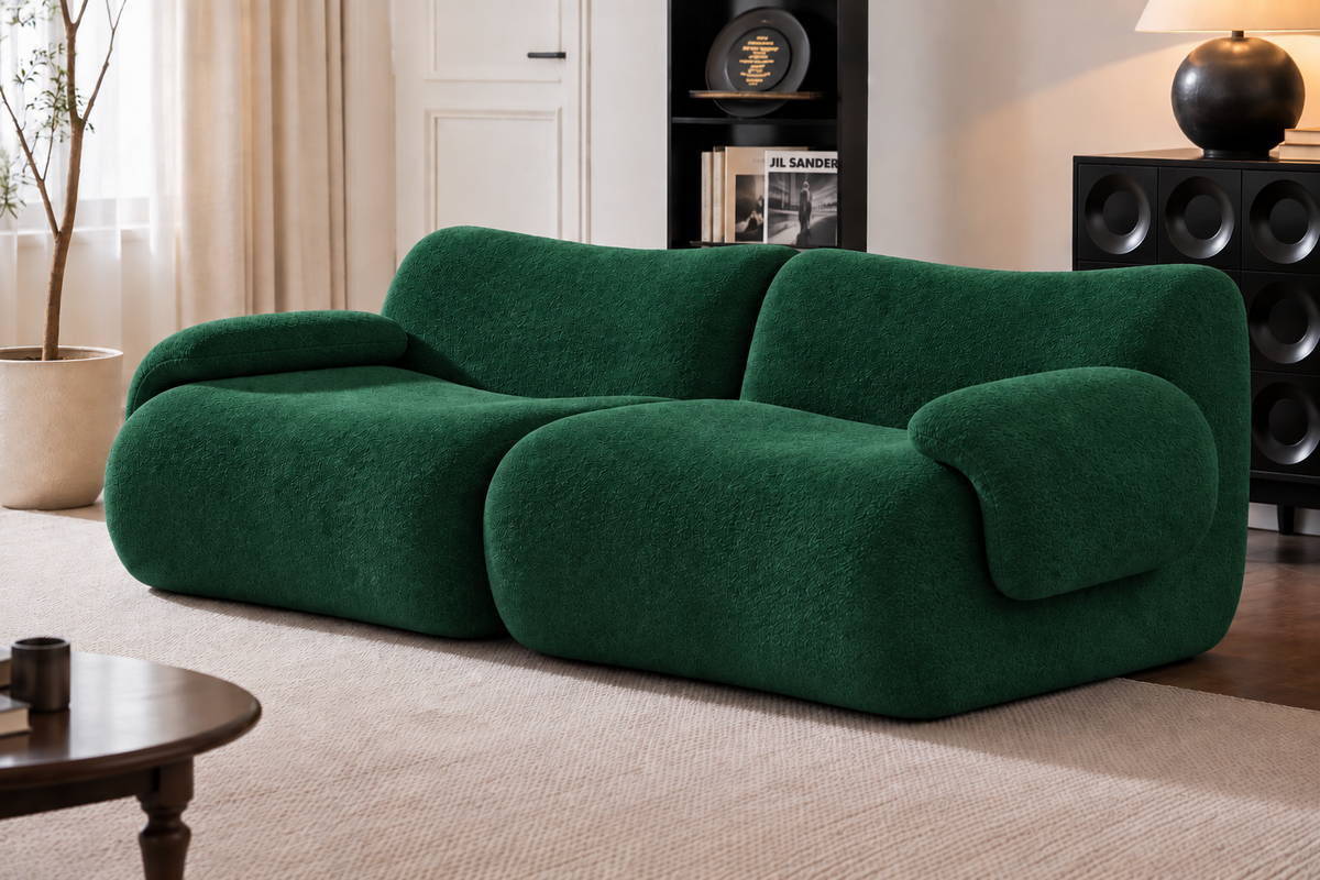 A modern, low-profile sofa upholstered in a textured dark green boucle fabric, styled in a contemporary living room setting with a beige rug, wooden coffee table, and shelving.