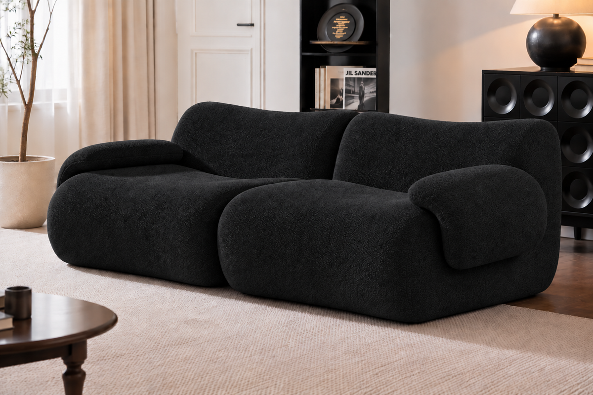 A modern black boucle sofa with rounded, organic shapes, set in a contemporary living room with a beige rug, wooden coffee table, and shelving.