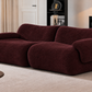A modern, low-profile sofa upholstered in a deep burgundy bouclé fabric, set in a styled living room with a beige rug, a potted plant, and a black sideboard.