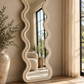 Ivory full-length wavy floor mirror with a sculptural organic frame in a sunlit beige interior