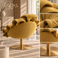 A plush oval accent chair upholstered in mustard yellow velvet with a ruffled backrest and a round brushed gold metal swivel base, shown in a styled interior. The right side includes four close-up detail panels highlighting the fabric texture and upholstery details.