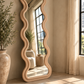 Rose full-length wavy floor mirror with a sculptural undulating frame against a textured beige wall
