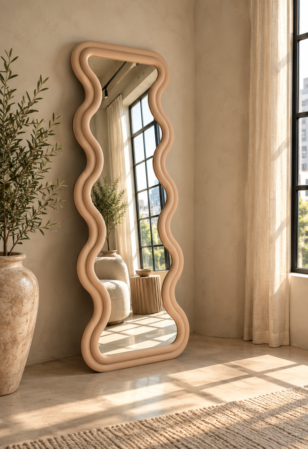 [color:rose] A full-length floor rose color mirror with a wavy, undulating frame in a warm pink finish, leaning against a textured beige wall in a sunlit room with a large ceramic planter and window curtains.