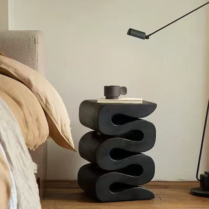 [color: black] Modern black side table with a cup on a wooden floor next to a beige armchair.
