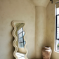 Ivory full-length wavy floor mirror with a scalloped sculptural frame against a beige plaster wall