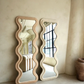 Ivory and rose full-length wavy mirrors with organic sculptural frames against a textured beige wall