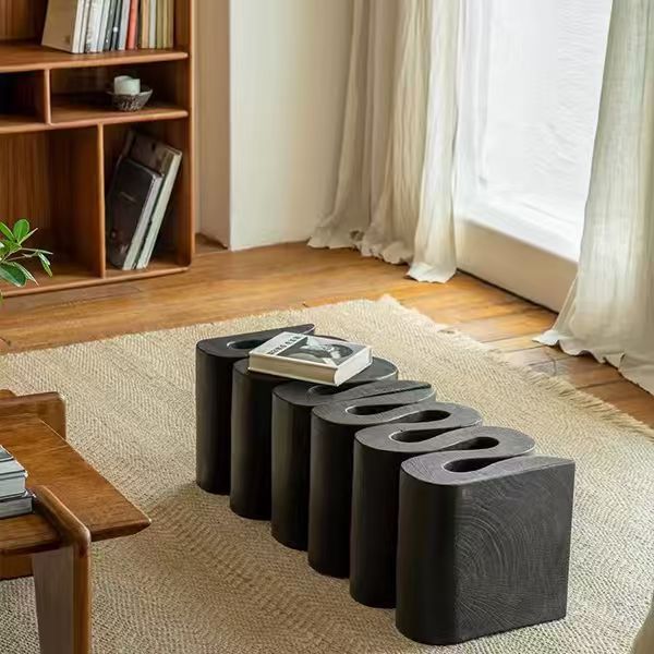 [color: black] Black stone stools in a living room setting with a wooden shelf and curtains.