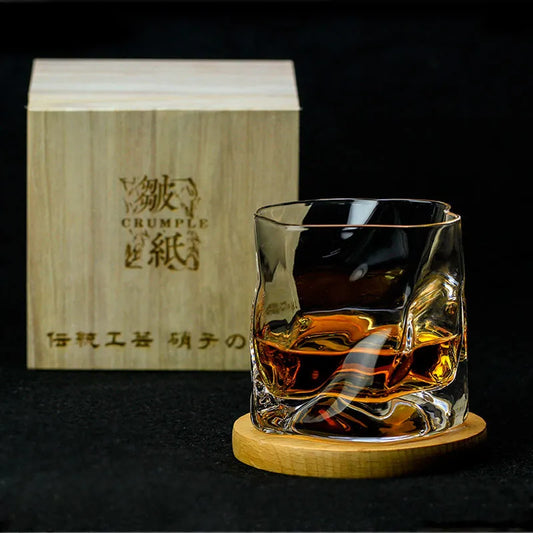 A glass of Lise Luxury Japanese Design Whiskey glass with a rich aroma on a wooden coaster with its packaging box in the background.