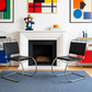 [color: noir] Two modern cantilever chairs with black leather seats and chrome steel S-curve bases, placed on a blue rug in front of a white fireplace in a styled living room.