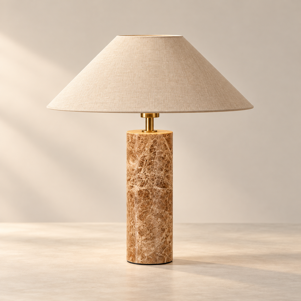 A table lamp with a tapered beige linen shade and a cylindrical polished stone base in warm tan and brown marbled tones, with a small gold-toned metal connector, shown on a light neutral surface against a soft beige background.