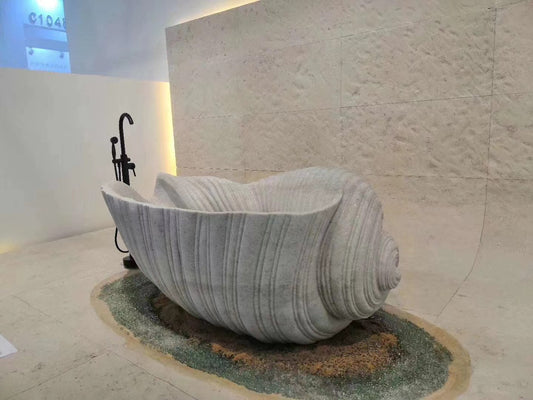 Stone sculpture of a Shell Marble Bath Tub placed indoors with pebble decoration and a wabi-sabi design principles-inspired black floor lamp beside it.