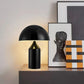 [color: black] Black table lamp on a wooden surface with framed art in the background