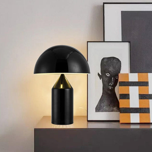 [color: black] Black table lamp on a wooden surface with framed art in the background