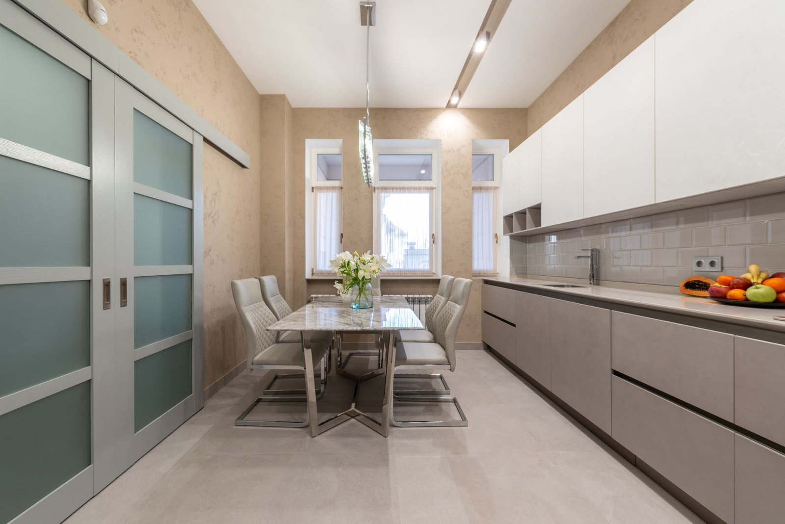 Bright dining area with pale table and chairs beside a glazed kitchen wall