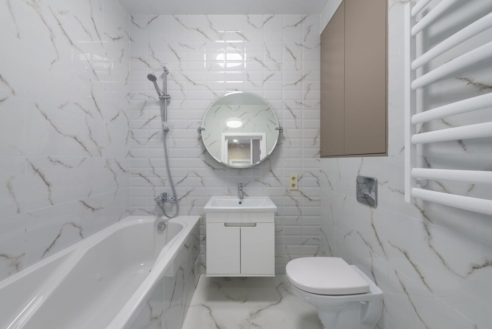 Bathroom with light veined walls, round mirror and white fitted bath
