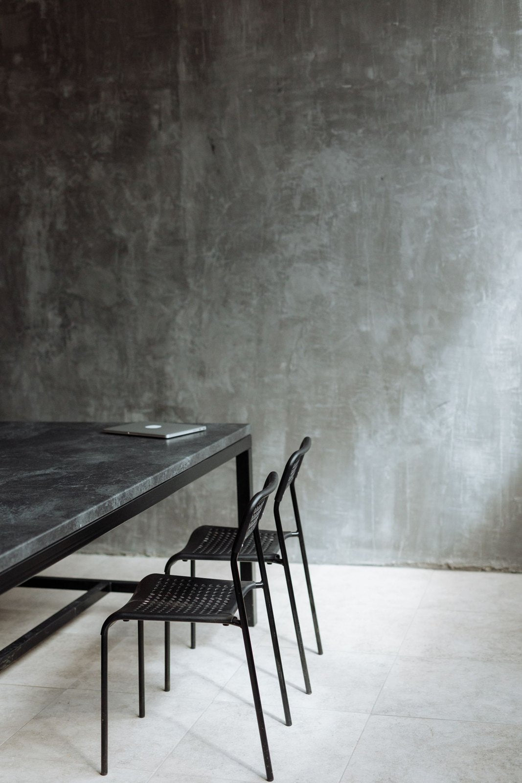 Dark veined table with slender metal chairs against a concrete wall