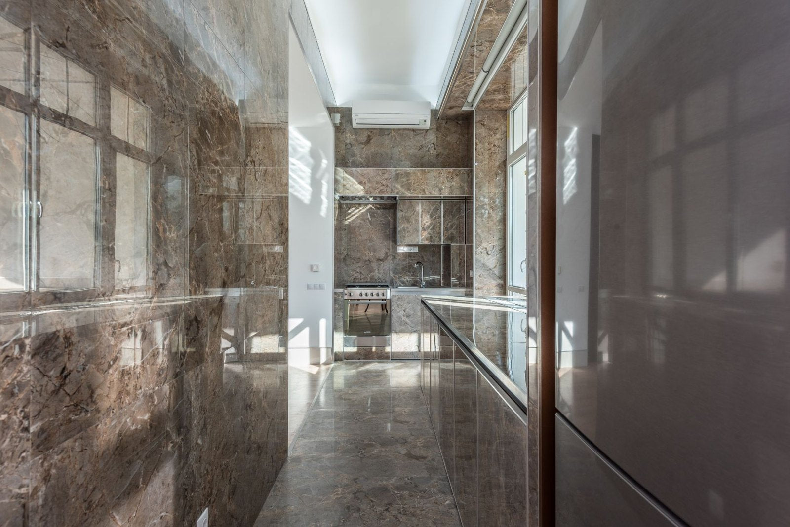 Long kitchen with large veined wall panels and daylight at the far end