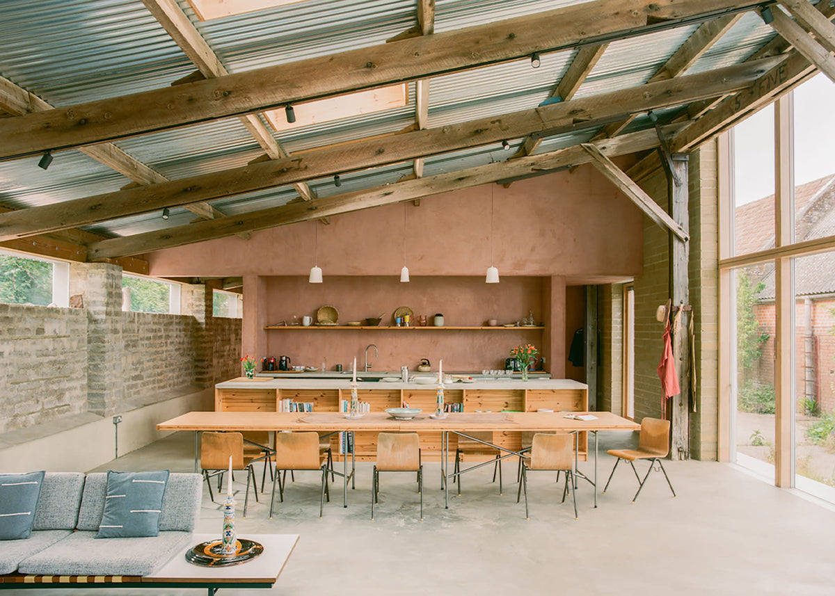 The open kitchen and dining space at South Barn sits beneath retained timber beams and corrugated roofing.